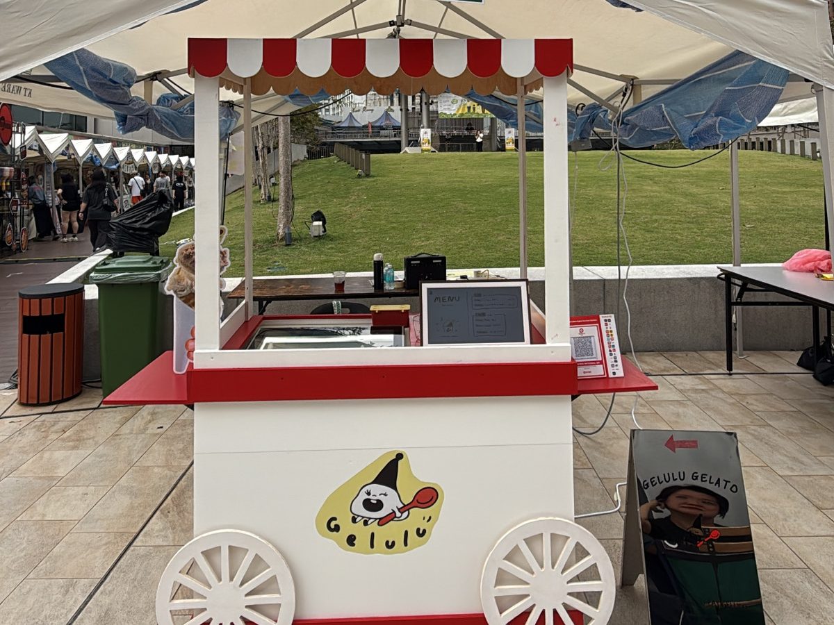 The Gelulu gelato cart under a canopy at an outdoor event, with the KL skyline behind